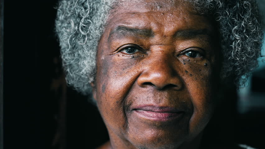 One serious black elderly lady looking at camera showcasing experience and wisdom. African American senior 80s woman with wrinkles and gray hair portrait face close-up