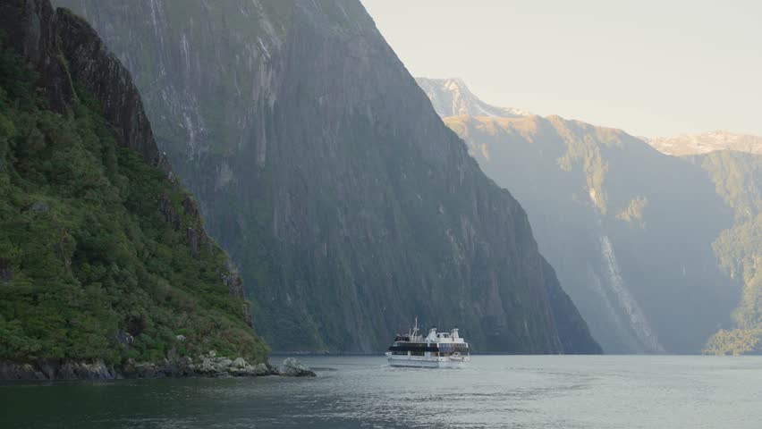 Ferry or tour boat sailing by the fiords of Milford Sound in New Zealand. Amazing landscape seen from ship. Picturesque scenery during winter in South Island. Tourism in nature by mountains and lakes