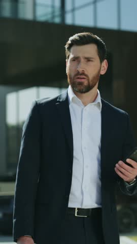 Smiling attractive two business men walking talking discussing on street in modern city near business center. Use phone hold cup of coffee. People around. Portrait. Slow motion