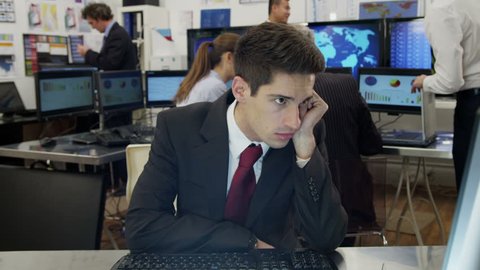 A very bored and tired  young businessman is struggling to stay awake at his desk while he is at work. As he lapses into sleep he looks around to check that his colleagues haven't noticed.