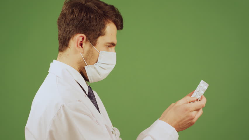 Masked doctor inspecting a blister pack of pills.