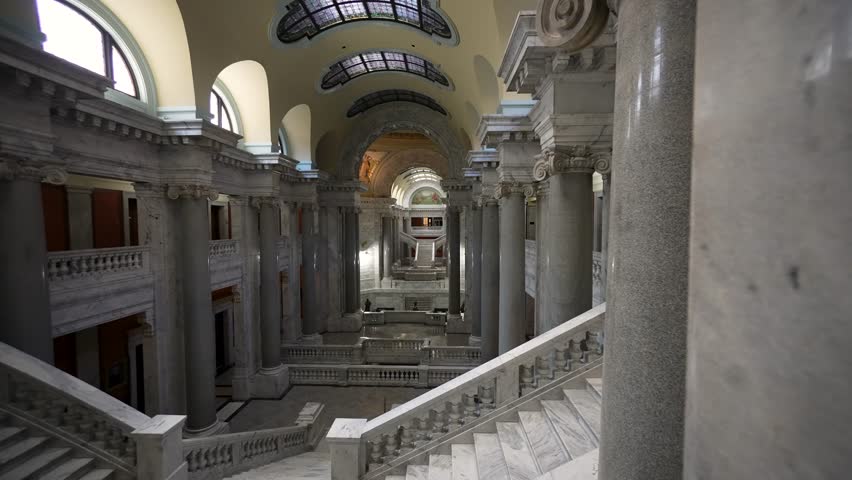 This magnificent interior showcases the Kentucky State Capitol in Frankfort, featuring marble columns, intricate murals, and a grand staircase lined with historic artistry.