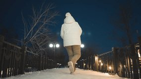 Choreographer dancing gracefully in illuminated snowy park walkway wearing white puffer coat and headphones under glowing lampposts and string lights with rhythmic hand movement expressing joy - Powered by Shutterstock - Get 15% off with code: PIKWIZARD15
