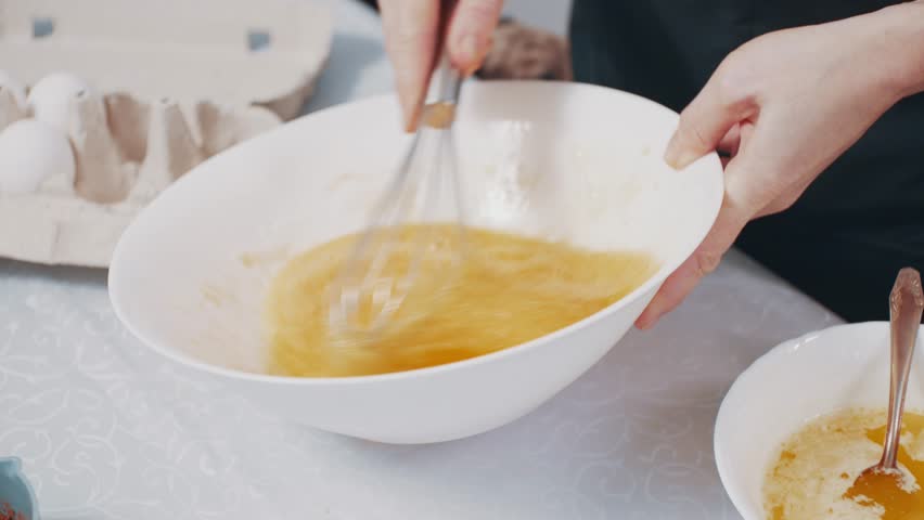 Woman preparing home-cooked food. Female beats eggs in a bowl in the kitchen at home. Close-up.