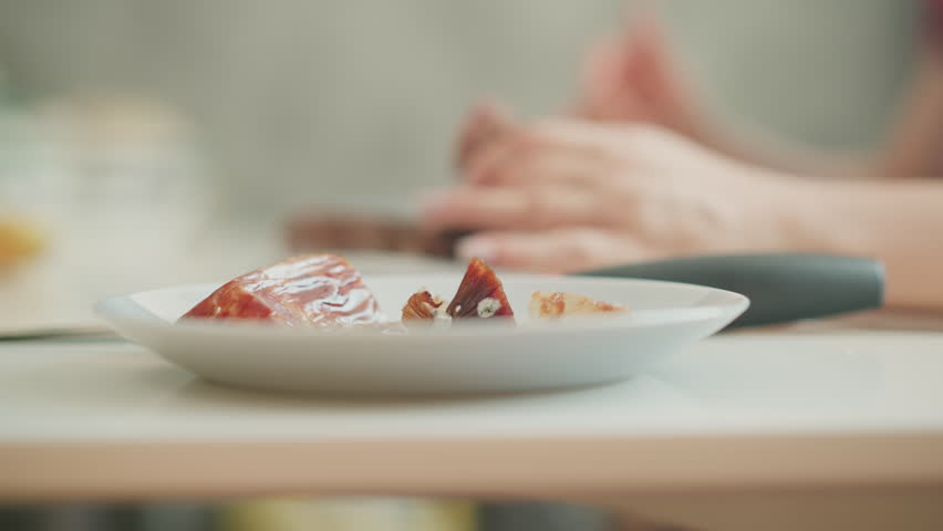 Blurred chef hands gently drop peeled sausage casing into white bowl on kitchen table, soft light and shallow focus create artistic mood for gourmet preparation and plating process