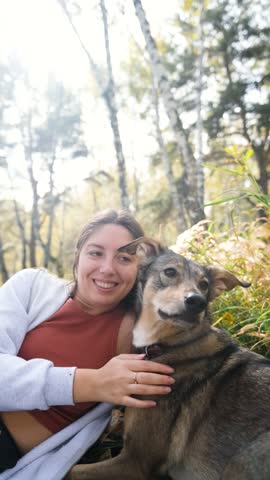 A young woman lies on the yellow autumn grass in the forest, in the fern leaves, her dog is walking next to her. A woman relaxes in nature while walking with her beloved dog