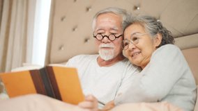 Happy Asian family senior couple relaxing and reading a book together on the bed in bedroom. Elderly husband and wife taking care each other. Retired people healthcare and mental health concept. - Powered by Shutterstock - Get 15% off with code: PIKWIZARD15