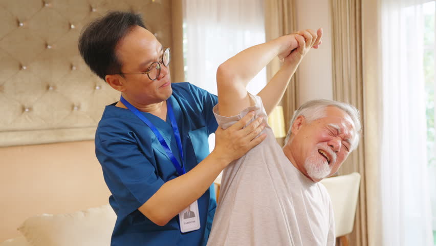 Asian senior man patient doing rehab physical therapy stretching muscle shoulder and arm with physiotherapist caregiver in bedroom. Home medical caregiving services and elderly people healthcare.