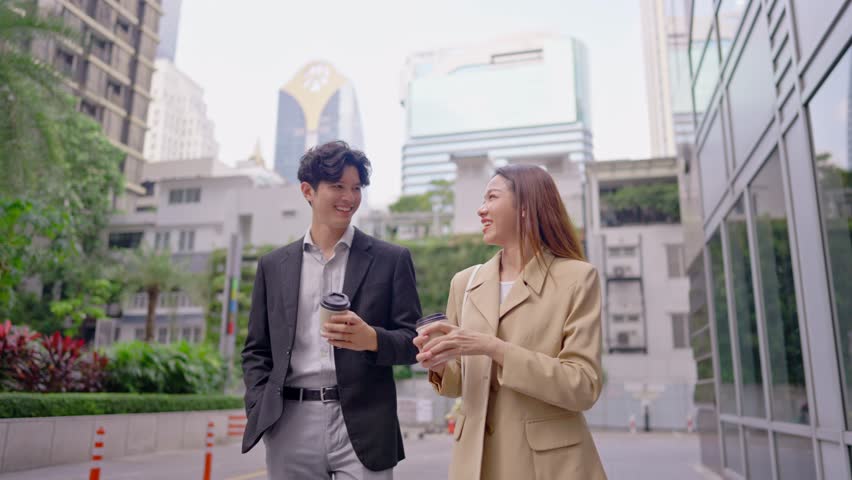 Asian young businessman and woman partner walking outdoors in the city. Attractive colleagues employee people feel happy and relax while spend time outside office company together with confidence.