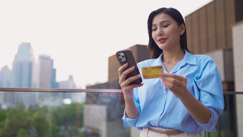 Asian woman using mobile phone shopping online outdoors in the city. Attractive young girl stand in urban setting, holding credit card and making online payment while purchasing goods from web store.