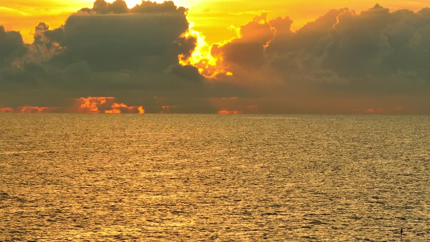 From above, the tropical ocean glows beneath a magnificent sunset, with clouds painted in fiery colors and the water shimmering in golden light, creating a captivating, epic natural view. Thailand.
