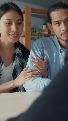 Vertical Screen : Happy asian young customer couple ready sign bank loan agreement for new house with broker agent, husband and wife consider finance investment insurance contract in front of broker.