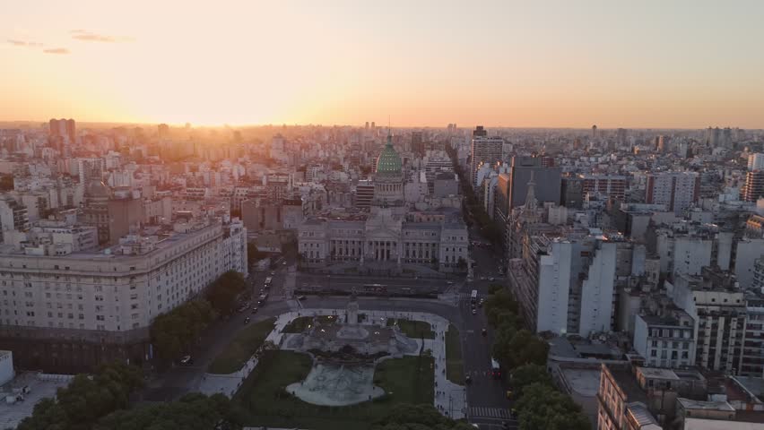 Aerial drone zoom out showing the National Congress of Argentina and surrounding plaza at sunset with the city expanding in all directions.