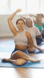 Smiling young female instructor leading group of women in Vinyasa yoga flow for body flexibility, transitioning from Gomukhasana with hands behind backs to Eagle arms of Garudasana in sunlit studio - Powered by Shutterstock - Get 15% off with code: PIKWIZARD15