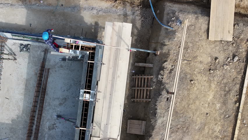 Highlighting a dynamic construction site where workers are actively engaged in tasks related to building a large structure. The camera captures a top-down perspective of the work area