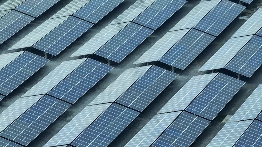 The aerial view captures a large array of solar panels, positioned in neat rows, symbolizing the growing commitment to renewable energy and the future of clean, sustainable power generation.
