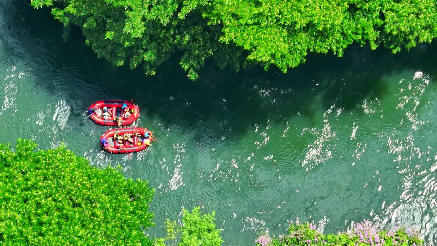 The aerial perspective illustrates the joy of exploring hidden rivers in a tropical jungle, with the raft and dense trees creating an immersive and adventurous journey through nature. Thailand.
