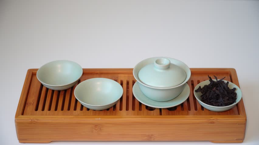 Cup or tea glass hot brew, he pours dried tea leaves into gaiwan on a wooden plate, placed on a wooden table, on a white background. Brewing Chinese tea in ceramic gaiwan during the tea ceremony. 