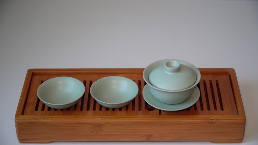 Cup or tea glass hot brew, he pours dried tea leaves into gaiwan on a wooden plate, placed on a wooden table, on a white background. Brewing Chinese tea in ceramic gaiwan during the tea ceremony. 