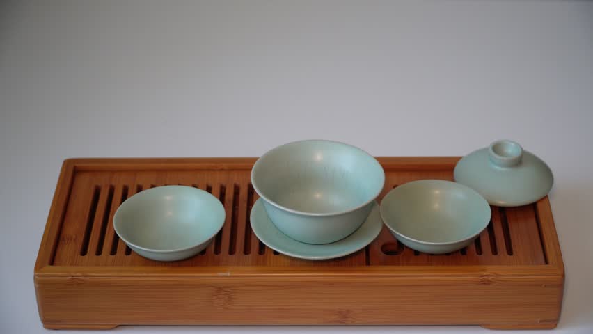 Cup or tea glass hot brew, he pours dried tea leaves into gaiwan on a wooden plate, placed on a wooden table, on a white background. Brewing Chinese tea in ceramic gaiwan during the tea ceremony. 