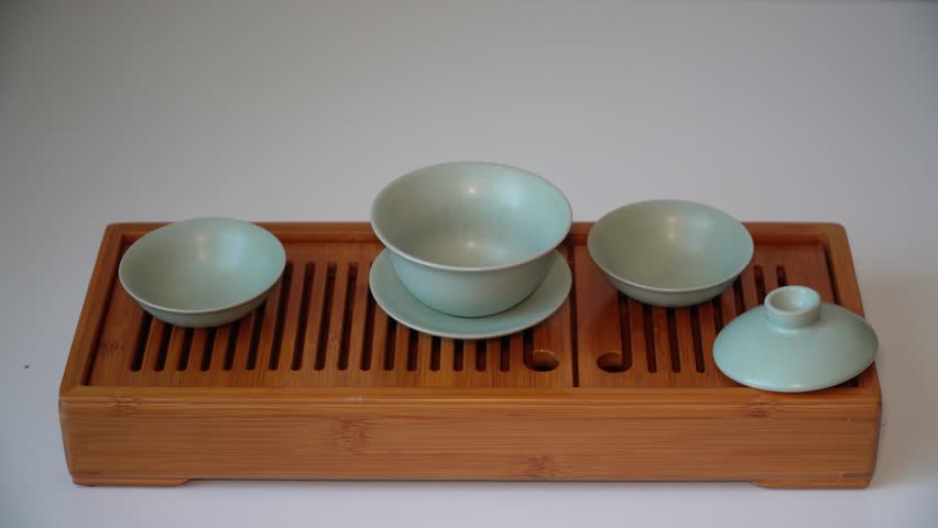 Cup or tea glass hot brew, he pours dried tea leaves into gaiwan on a wooden plate, placed on a wooden table, on a white background. Brewing Chinese tea in ceramic gaiwan during the tea ceremony. 