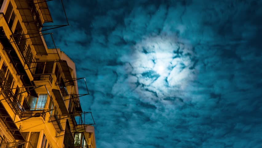 Beautiful time-lapse of stars and moon shining through clouds over a cityscape at night