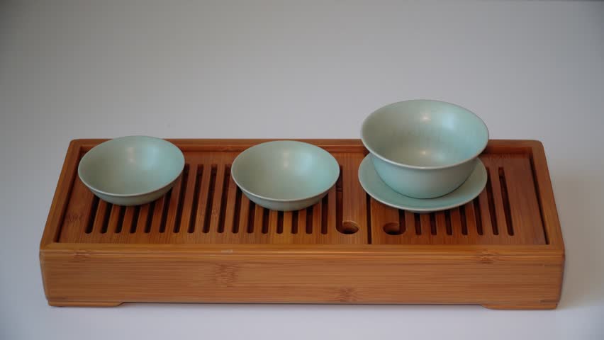 Cup or tea glass hot brew, he pours dried tea leaves into gaiwan on a wooden plate, placed on a wooden table, on a white background. Brewing Chinese tea in ceramic gaiwan during the tea ceremony. 