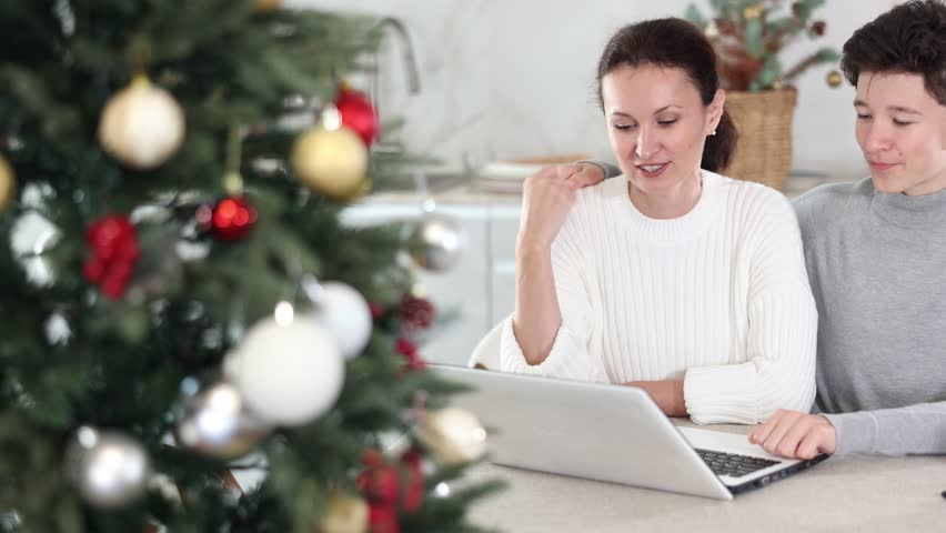 Positive mother and teenage son talking at home via video conference during Christmas celebration. High quality 4k footage