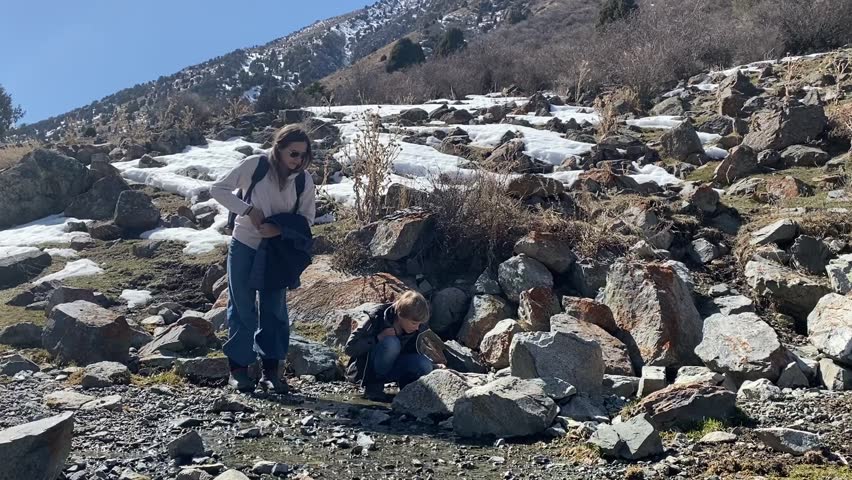 Mother and child exploring rocky mountainside with melting snow