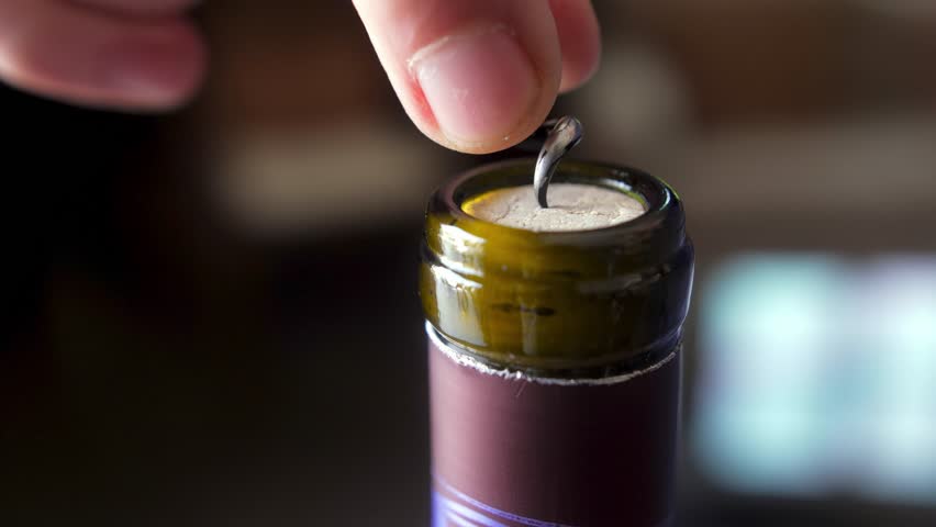 close-up shot of a corkscrew being inserted into a wine bottle's cork, capturing the moment of opening with hands holding the bottle steady.