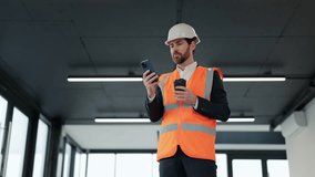 Successful architect in formal suit and hard hat enjoys coffee break, browsing on smartphone in building under construction. Positive emotions, good mood, relaxation, break. - Powered by Shutterstock - Get 15% off with code: PIKWIZARD15
