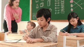 Asian smart boy smiling to camera while student writing answer in answer sheet. Multicultural student doing classwork or test while caucasian teacher checking student homework at classroom. Pedagogy. - Powered by Shutterstock - Get 15% off with code: PIKWIZARD15