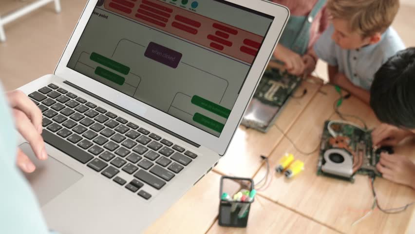 Top view of smart caucasian teacher coding engineering prompt and generated AI while diverse children learning main board. Group of diverse student working together and fixing main board. Pedagogy.