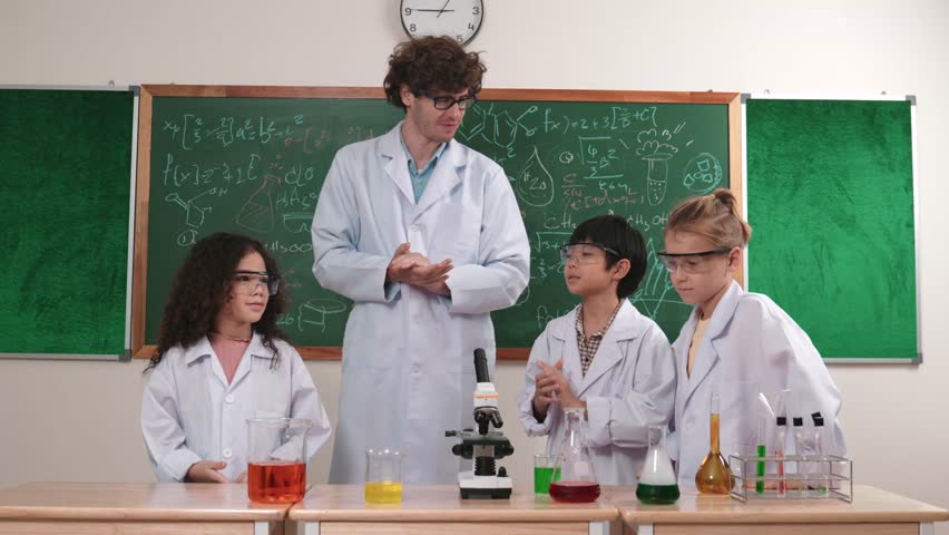 Smart science teacher teach about science theory to diverse child while happy elementary student listening and learning about chemistry liquid on table with microscope and colored solution. Pedagogy.