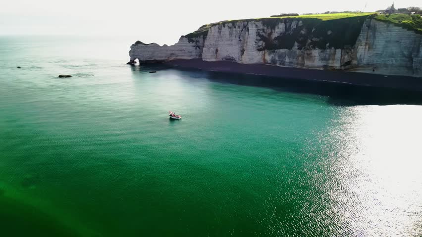 Fishing boat at rocky shores in the sun. White fishing boat off the coast of France against the backdrop of high cliffs of Etreta.