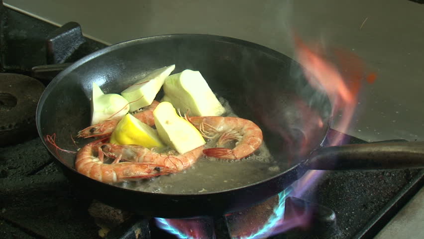 Hokianga, New Zealand. April 2013. Chef prepares prawns in pan over gas hob,