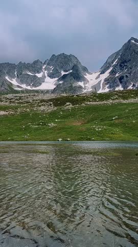 A mountain range with a lake in the foreground. The water is calm and the mountains are covered in snow