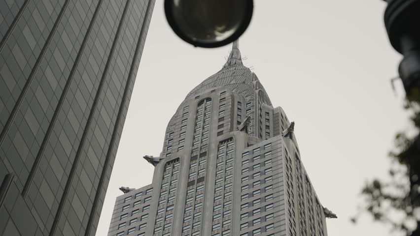A close-up upward view of the iconic spire and top section of the Chrysler Building, captured from below. Showcasing its distinctive Art Deco architecture against the New York City skyline.