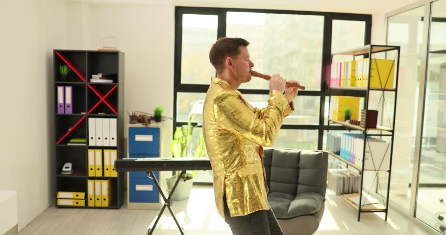 Skilled musician dressed in golden jacket plays flute melody at break in office. Talented man performs mesmerizing flute tune masterfully. Slow motion