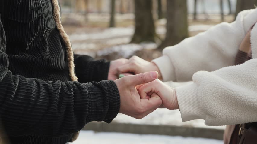 Happy couple in love walking together outside in a winter park. Husband and wife warming each other's hands.