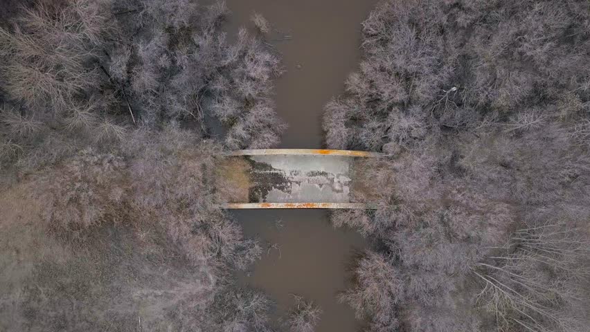 Top down aerial descends to abandoned bridge over grey river water