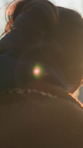 A tearful girl walking through a park at sunset, wearing a brown coat and a hoodie. The close-up shot emphasizes her emotional state, with the soft, golden light downcast her face