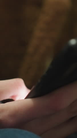 Close-up of a hand wearing a brown coat and blue jeans, holding and scrolling through a smartphone, the fingers interacting with the device, capturing a moment of quiet contemplation