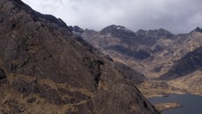 Drone reveal of Loch Coruisk on the Isle of Skye, showing shifting light across rugged terrain and thick cloud cover trailing over dramatic mountain peaks - Powered by Shutterstock - Get 15% off with code: PIKWIZARD15