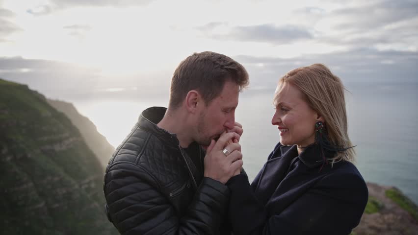 Romantic couple holding hands on cliff at sunset