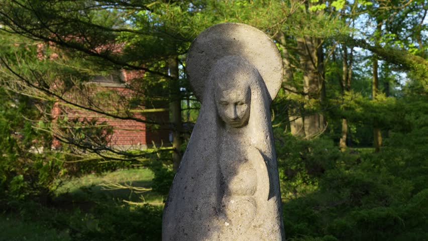 A close-up shot of a stone statue representing the Virgin Mary, located in the Central Cemetery in Szczecin. Surrounded by greenery and bathed in soft light. Shot handheld, no stabilization used.