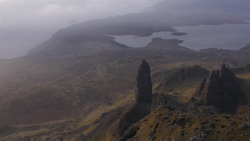 Serene drone shot of the Old Man of Storr on the Isle of Skye in warm morning light, with soft haze and distant clouds casting a dreamy mood across the Highland landscape