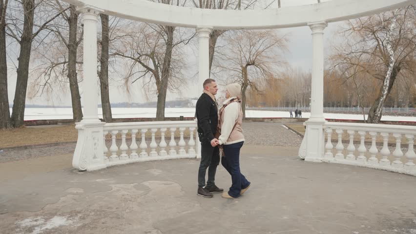 Happy couple in love are having a great time in a winter park near the lake. Man and woman are hugging and kissing