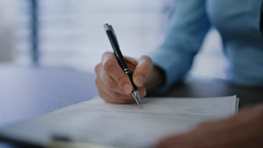 Businesswoman hand signing contract holding pen at office desk closeup. Unrecognizable woman manager putting signature on legal paper at workplace. Lady executive legalize financial agreement indoors.