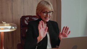 A senior businesswoman finishes a video call, smiles and waves gently to the screen. Her gesture of farewell adds a warm, human touch to the professional interaction. 4k footage - Powered by Shutterstock - Get 15% off with code: PIKWIZARD15